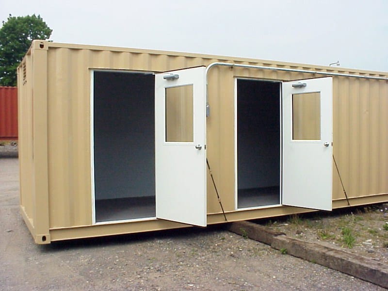 Tan A-Verdi storage container with two open white entry doors, featuring spacious interior access and sturdy steel construction on a gravel surface under overcast skies