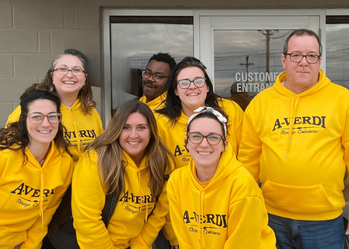 A-Verdi team members smiling in matching yellow branded hoodies outside the customer entrance.
