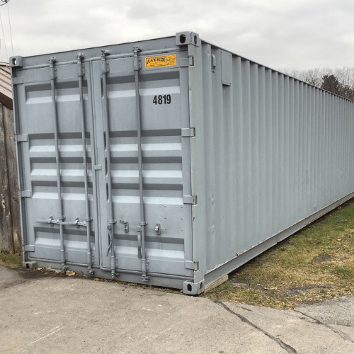 Reconditioned Container A clean, gray A-Verdi storage container labeled "4819" positioned on a concrete and grass surface near a wooden fence. The container is in good condition with a yellow A-Verdi identification plate above the doors under an overcast sky.