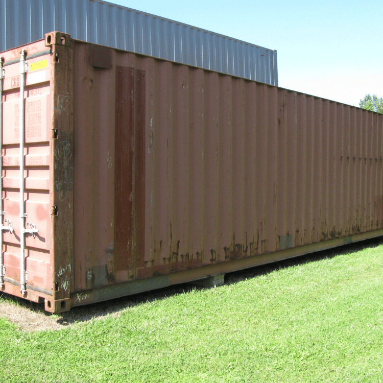 Large rusty brown 40-foot shipping container placed on grass, showing corrugated steel sides and closed double doors.