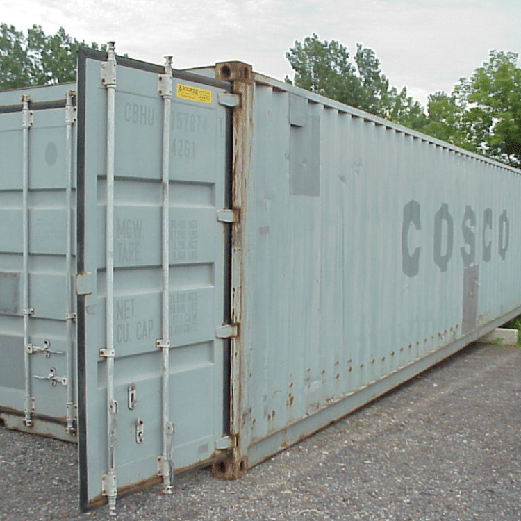 A light gray A-Verdi storage container with the brand "COSCO" faintly printed on the side is shown with one door partially open. The container has visible rust along the door edges and lower panels. A yellow A-Verdi label is located near the top of the door. The container is placed on a gravel surface with trees and cloudy sky in the background.