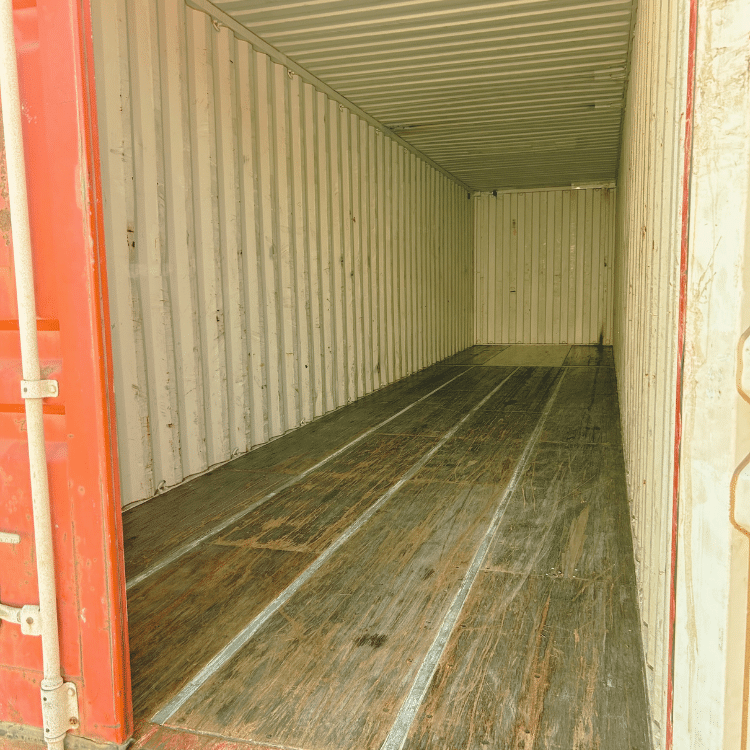 40' Sale Container Inside-View Interior view of an empty shipping container with a red door frame, showing clean metal walls and a worn wooden floor. Natural light illuminates the long, rectangular space, emphasizing the container’s depth and storage capacity.
