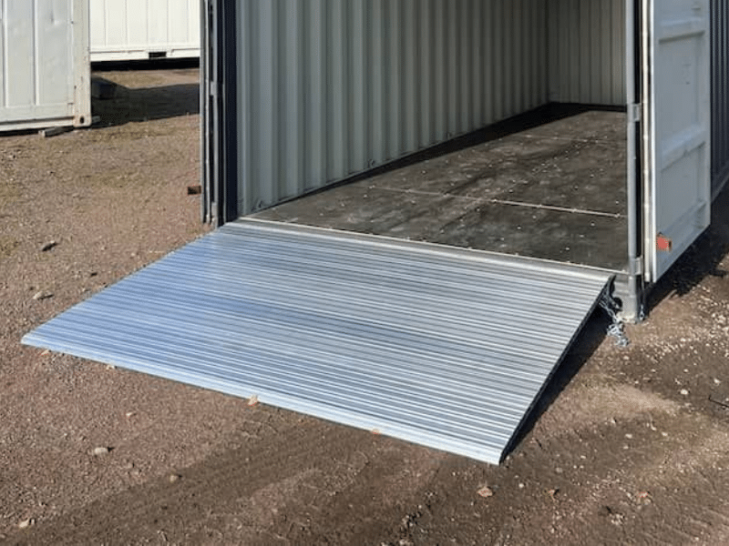 Open storage container with a silver metal loading ramp extended to the ground, providing easy access for loading and unloading.