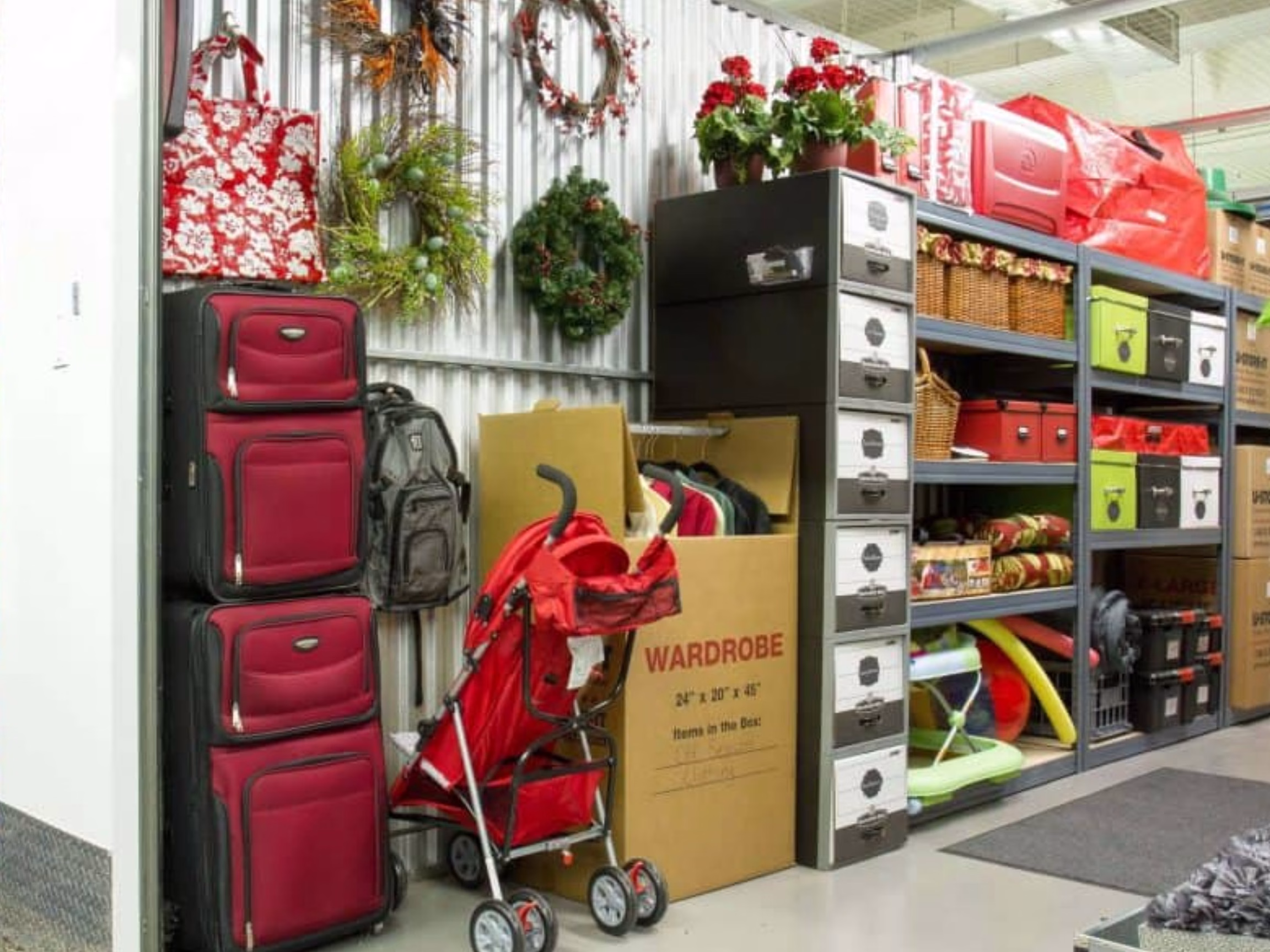 Self storage unit with organized household items including luggage, wardrobe box, stroller, filing cabinets, and storage bins.