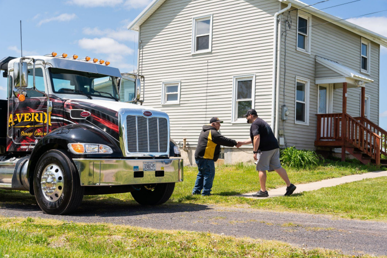 A-Verdi truck driver shaking hands with a homeowner in front of a residential house, symbolizing friendly service and customer satisfaction.