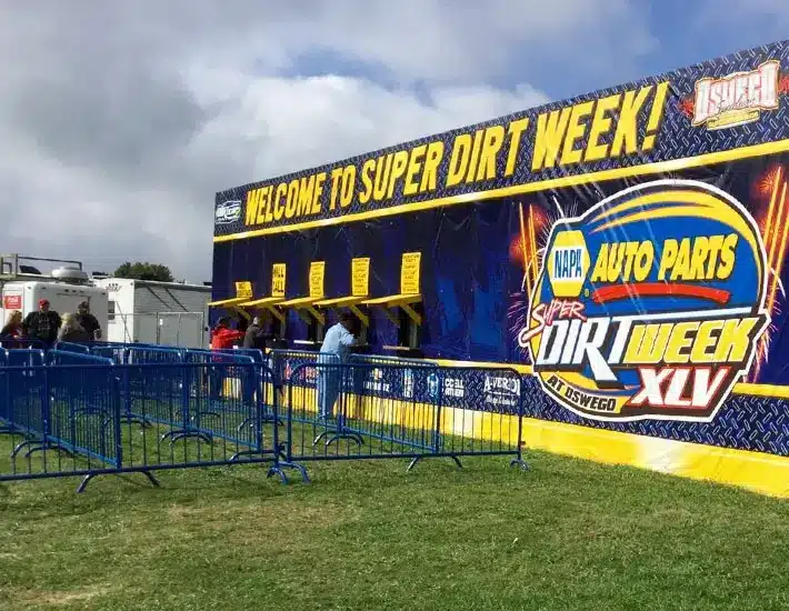 A-Verdi Containers Power Major Events – From Ticket Booths to Storage, We’ve Got You Covered! This image shows the Super DIRT Week ticketing area, with a large branded banner and multiple service windows set up using modified containers. Blue crowd control barriers organize the lines for attendees.
